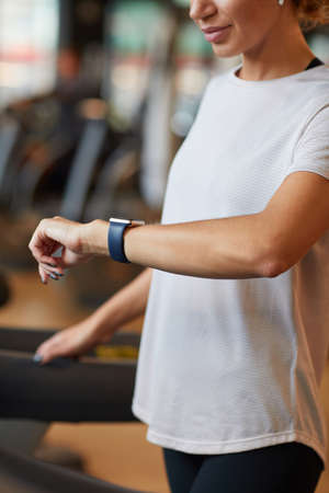Close-up of healthy woman looking at watch on her arm and checking her pulse while training on...
