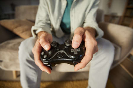 Close-up of gamer using joystick while sitting on sofa and playing computer games