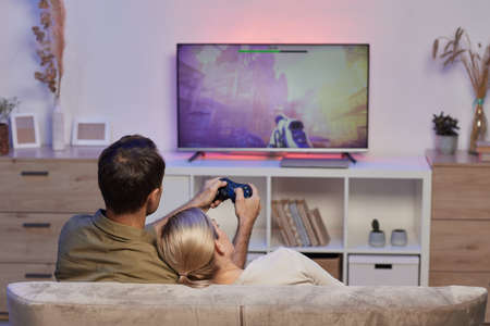 Rear view of young couple resting on sofa in the living room and playing video game