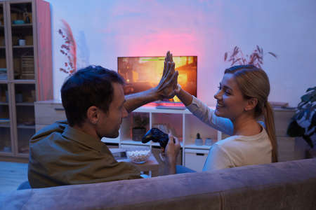 Young happy couple sitting on sofa and giving high-five to each other while playing the video game at homeの写真素材