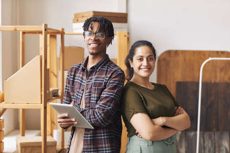 Portrait of two colleagues standing with arms crossed back to back and smiling at camera they...