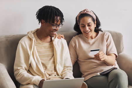 Young woman showing the number of her credit card to her boyfriend who using laptop they shopping...