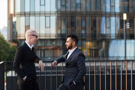 Business people talking to each other standing on balcony against the modern buildingsの写真素材