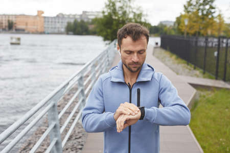 Young man checking his pulse on fitness bracelet during his jogging in the park