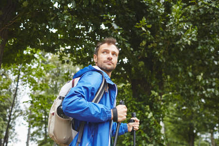 Portrait of young man with backpack behind his back using sticks for sport walking outdoorsの写真素材