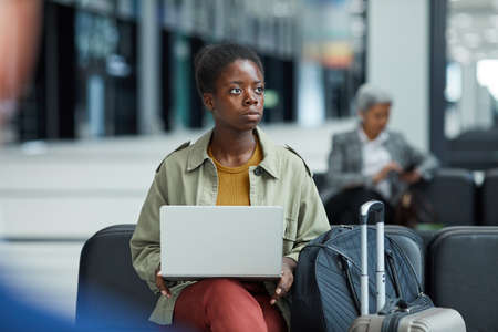 African young woman using her laptop computer while sitting and waiting for her flight at the airportの写真素材