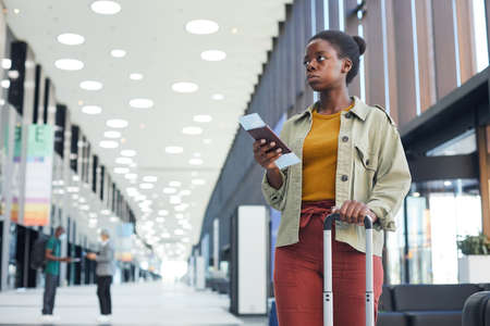 African woman with luggage and tickets standing at the airport and waiting for her flightの写真素材