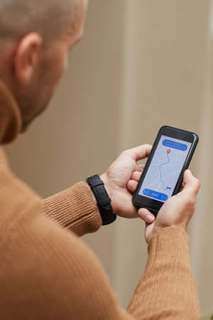 Rear view of man holding mobile phone and following for the car on the map he waiting for the taxi