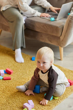 Cute baby boy sitting on the floor and playing with colorful blocks in the roomの写真素材