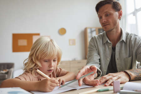 Teacher sitting at the table with his pupil and explaining hime the new topicの写真素材