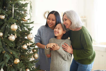 Asian happy family looking at their decorated Christmas tree in the roomの写真素材