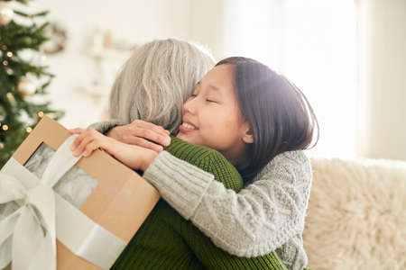 Mother embracing her little daughter and congratulating her with Christmas Day at homeの写真素材