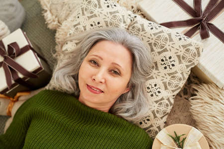 High angle view of mature woman lying on pillow among presents resting and looking at cameraの写真素材