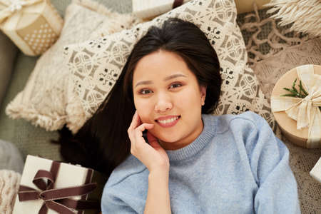 Portrait of Asian young woman with dark hair smiling at camera while resting on the floor among...
