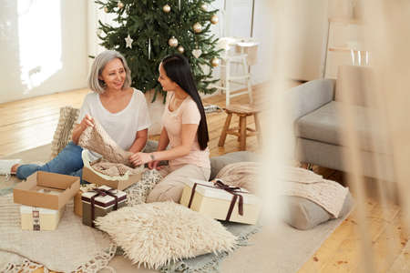 Asian beautiful mother opening Christmas presents together with her daughter on the floor in the roomの写真素材