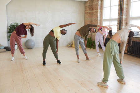 Group of people standing and exercising together with instructor in health club