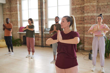 Young instructor showing the exercises to the group during yoga class in health club