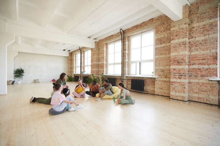 Group of young dancers sitting on the floor resting and talking in dance studioの写真素材