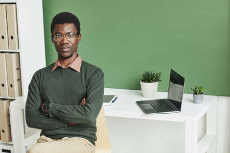 Portrait of African businessman in casual clothing standing with arms crossed at office and looking...