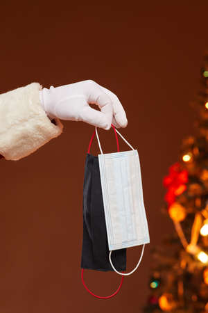 Close-up of man in glove holding protective masks with Christmas tree in the background