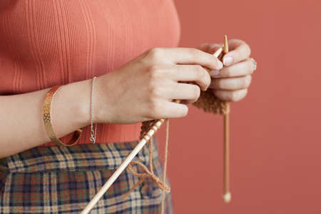 Close-up of woman holding knitting needles she knitting for herself standing against the pink...