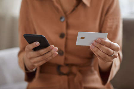 Close-up of woman holding mobile phone and credit card in her hands she paying online for billsの写真素材