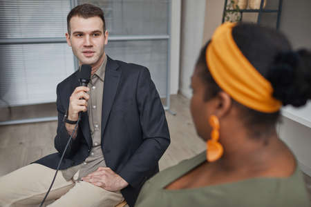 Young TV reporter with microphone interviewing African woman at office