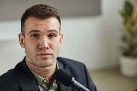 Portrait of young business speaker looking at camera while sitting at business conference