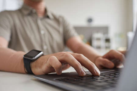 Close-up of man sitting at the table and typing on computer keyboard communicating online