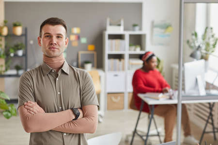 Portrait of young business leader standing with arms crossed and looking at camera at office with...