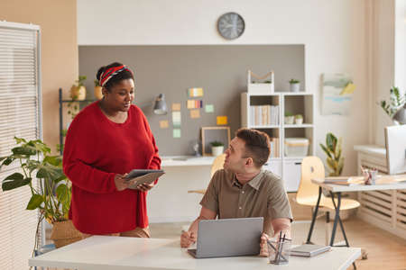 African businesswoman using tablet pc and talking to her colleague while he using laptop they...