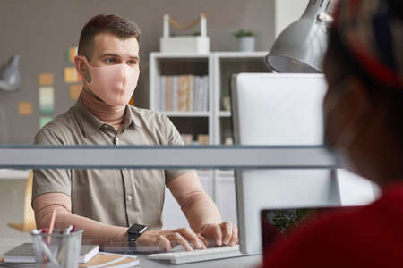 Young man in protective mask working at his workplace at office
