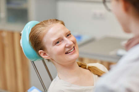 Young woman sitting on dental chair and smiling to doctor during her visit in dental clinic