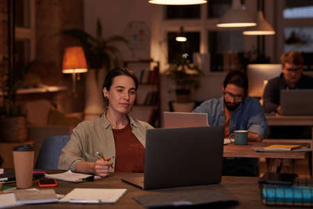 Young businesswoman sitting at the table in front of laptop and looking at monitor working at office