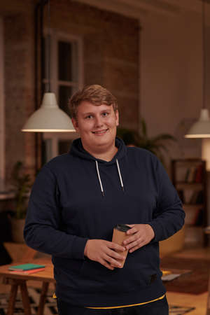 Portrait of young overweight businessman in casual clothing drinking coffee and smiling at camera...