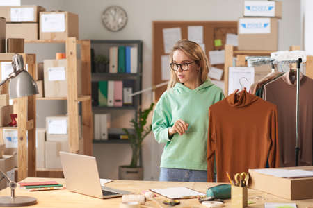 Young designer showing her clothes during online conference on laptop at modern office