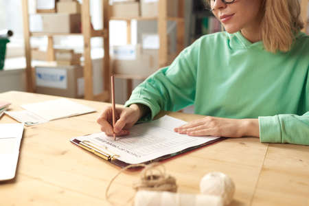Close-up of young woman sitting at the table and writing plans in her document