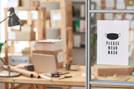 Image of advert with text to wear mask hanging on glass wall at officeの写真素材