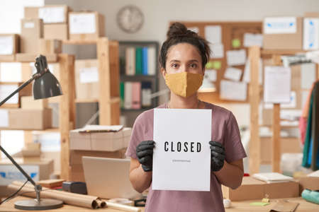 Portrait of young woman in protective mask holding placard in her hands while standing at officeの写真素材