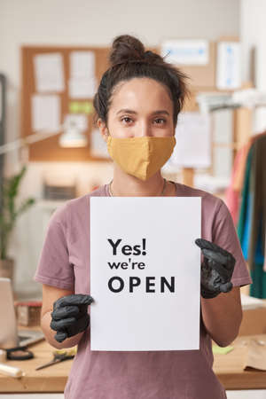 Portrait of young woman in protective mask holding placard while standing at officeの写真素材