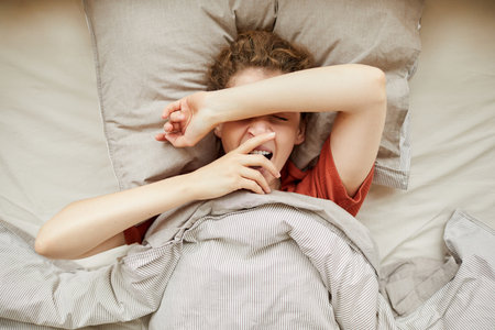 High angle view of young woman lying in her bed and yawning waking up in the morning