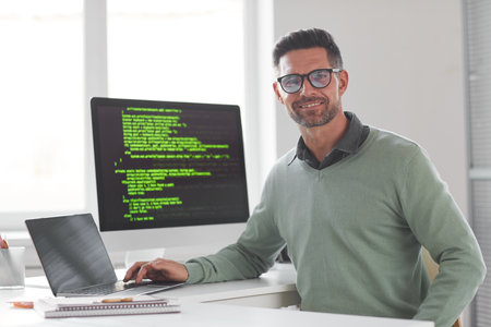 Portrait of mature computer programmer in eyeglasses looking at camera while developing new computer systemの写真素材
