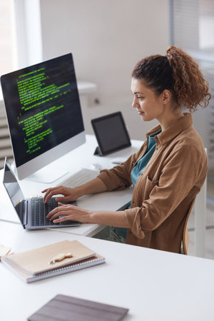 Young woman sitting at the table and concentrating on online work on laptop working at computer...