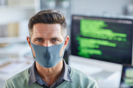 Portrait of young man in protective mask looking at camera while working at officeの写真素材