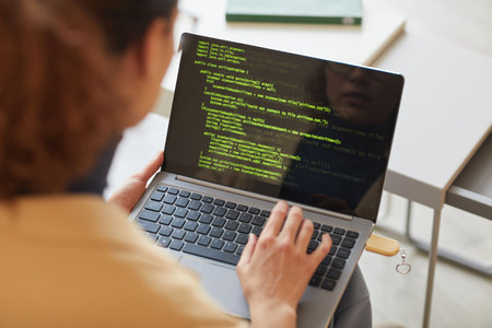 Rear view of female software programmer typing codes on laptop working with new softwareの写真素材