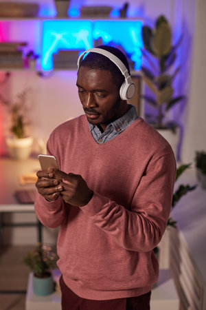 African young man in wireless headphones listening to music online on his mobile phone