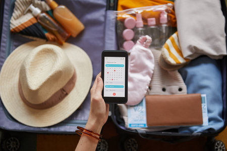Close-up of woman looking at calendar in her mobile phone while packing clothes in vacationの写真素材