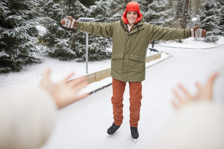 Happy young man in warm clothing skating on skating rink in winter in the park