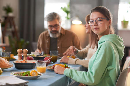 Portrait of teenage girl looking at camera while having dinner with her family at homeの写真素材