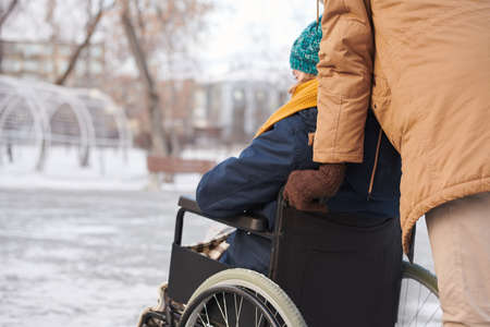 Rear view of disabled woman walking in the park in winter with her friend